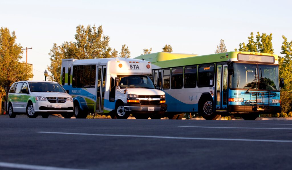 A bus, paratransit van, and rideshare car from Spokane Transit Authority are lined up on a road during the day.