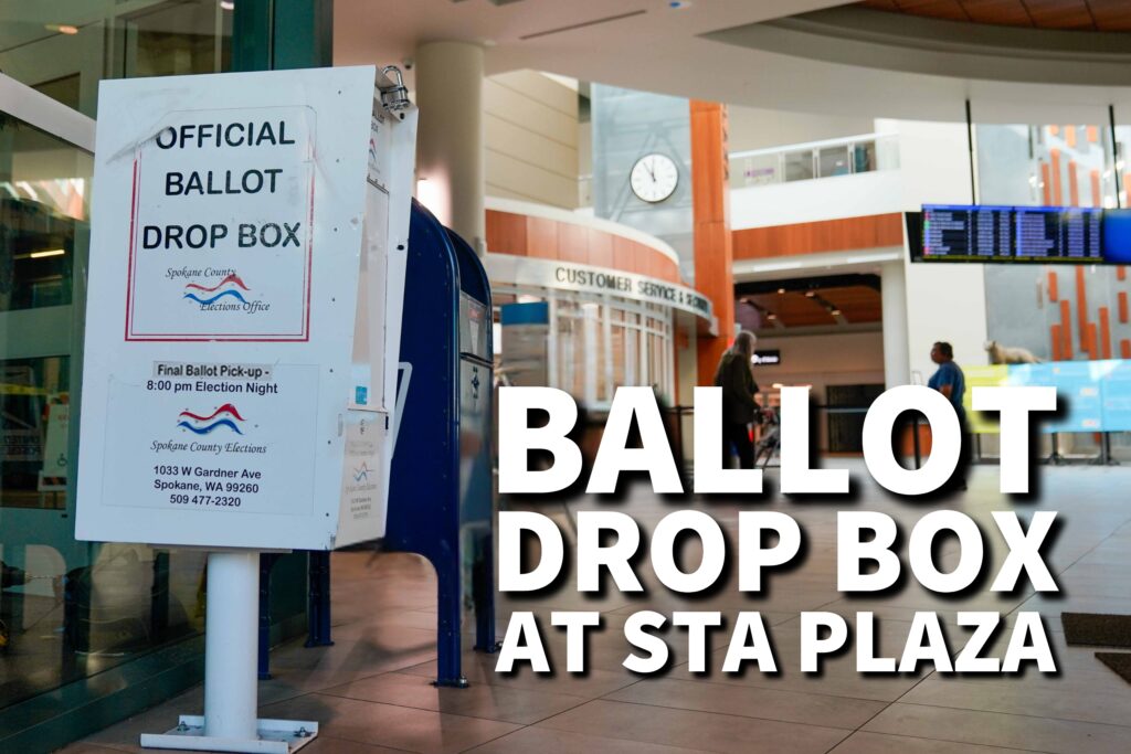 A ballot drop box at STA Plaza with signs indicating official ballot drop-off and an interior of a transit center in the background.