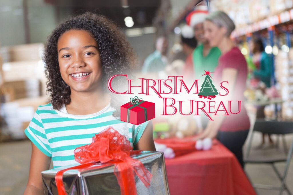 Girl smiling with a gift, standing in a festive setting with "Christmas Bureau" text overlay and people in the background.