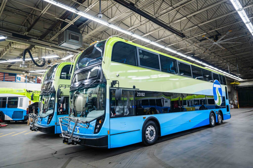 A pair of blue and green double-decker buses parked in a spacious indoor garage.