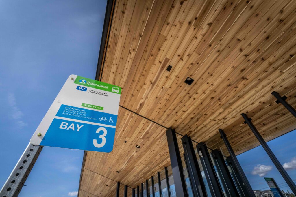 Bus stop sign for Bay 3 under a modern wooden roof, with blue sky in the background.