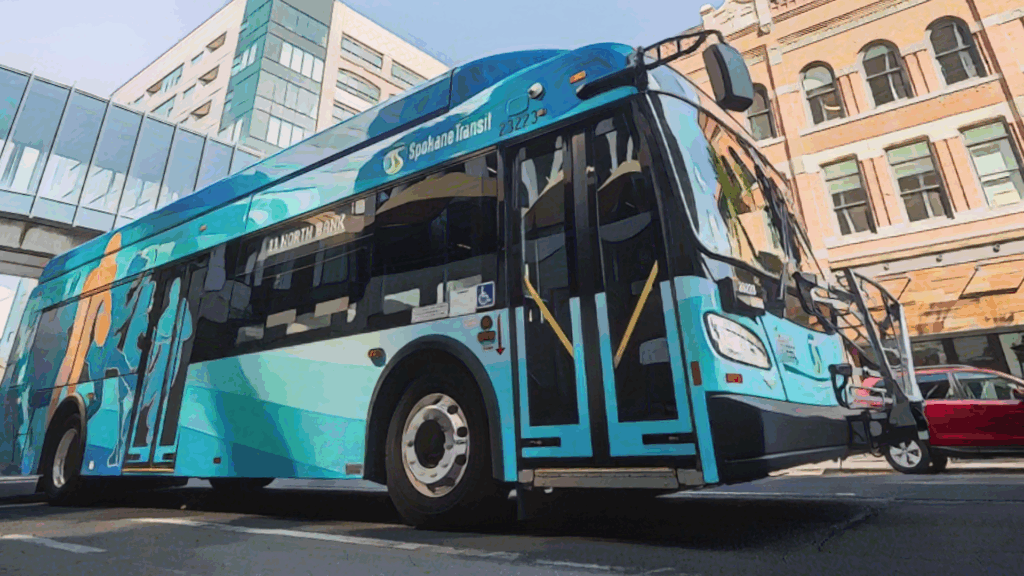 Spokane Transit bus with blue and teal design parked on city street near modern and historic buildings.
