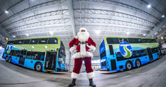 Santa Claus standing in front of two STA double-decker buses inside the Boone NorthWest Garage