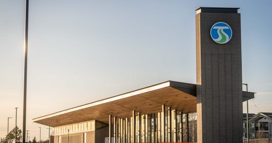 Modern building with large windows and a tall signpost under a clear sky, featuring a blue and green logo.