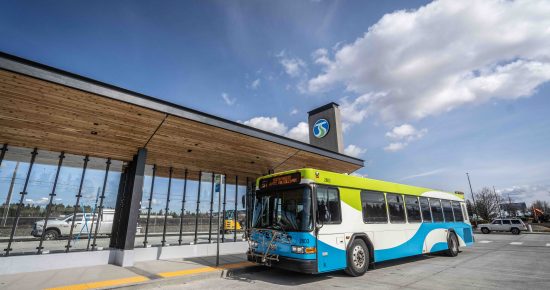 A blue and green bus parked at a modern transit station under a partly cloudy sky.